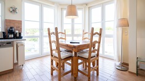 Een eetruimte met een houten tafel en stoelen, een koffiezetapparaat en uitzicht door grote ramen.
