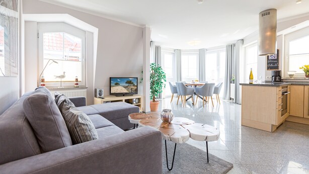 Ein modernes Wohnzimmer mit einem grauen Sofa, einem Couchtisch und einem Essbereich mit Tisch und Stühlen.