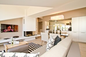 Ein modernes Wohnzimmer mit einer Couch, einem Couchtisch und einem Fernseher. Es gibt eine Küchenzeile mit Schränken und einem Esstisch.