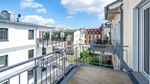 Un immeuble résidentiel à plusieurs étages, doté de balcons et d’une terrasse en bois, avec un ciel bleu dégagé.