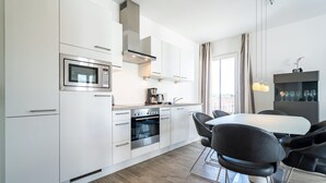 Une cuisine moderne avec des meubles blancs, un four encastré, un four à micro-ondes et un coin repas comprenant une table et des chaises.