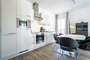 Una cocina moderna con armarios blancos, horno empotrado, microondas y un comedor con mesa y sillas.
