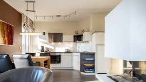 Ett modernt kök med vita skåp, en inbyggd ugn och en mikrovågsugn. Det finns en matplats med ett bord och stolar, och en öppen spis med en omramning av sten.