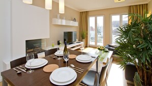 A modern dining area with a wooden table set for four, a television, and a large window with curtains.