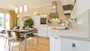 A modern kitchen with a built-in oven, a dining area with a table set for four, and a view of the city through the window.