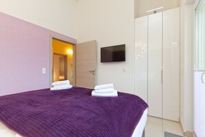 Un dormitorio con una colcha morada, un televisor de pantalla plana en la pared y un armario.