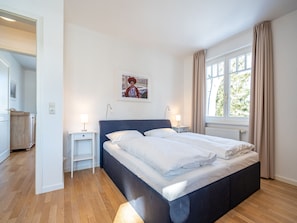 Ein Schlafzimmer mit einem Bett, Nachttischen, einem Fenster und einer Tür zu einem anderen Raum.