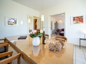 Uma sala de jantar com uma mesa de madeira, cadeiras, um vaso com flores, uma garrafa e bolas decorativas.