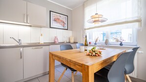 A modern kitchen with white cabinets, a wooden dining table, and a window with a view of the city. - Seeresidenz Haus Atlantic, App. C02 (Heringsdorf)