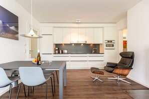 Een moderne keuken met witte kasten, een inbouwoven en een eethoek met een tafel en stoelen.