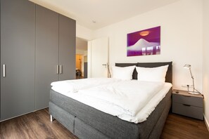 Een moderne slaapkamer met een groot bed, een grijze inbouwkast en een schilderij aan de muur.