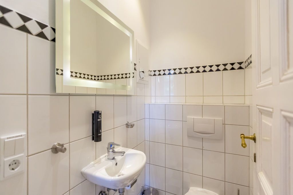 A bathroom with white tiles, a sink, a mirror, and a toilet.