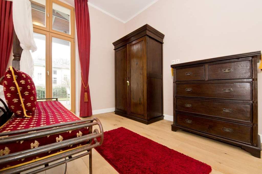 A room with a bed, a wooden wardrobe, a red rug, and a window with curtains.