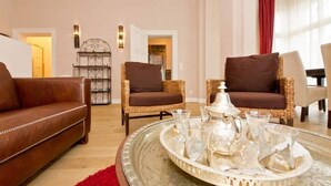 A living room with a brown leather sofa, two wicker armchairs, a coffee table with a tray of glassware, and a decorative metal shelf. - Villa Julius, App. 4 Marrakech (Heringsdorf)