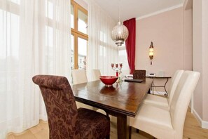A dining area with a wooden table, white and patterned chairs, a red bowl, and a decorative hanging light.