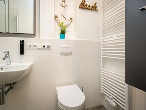 Ein Badezimmer mit weißem Waschbecken, Toilette, Handtuchhalter und Wandspender für Handtücher.