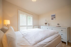 Un dormitorio con cama, mesita de noche, lámpara, cómoda y ventana con persianas.