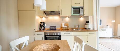 A modern kitchen with light-colored cabinets, a microwave, and a coffee maker. There is a wooden table with a woven placemat and white chairs.