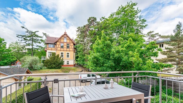 Ein Balkon mit Tisch und Stühlen, der auf ein Wohngebiet mit Häusern und Bäumen blickt.