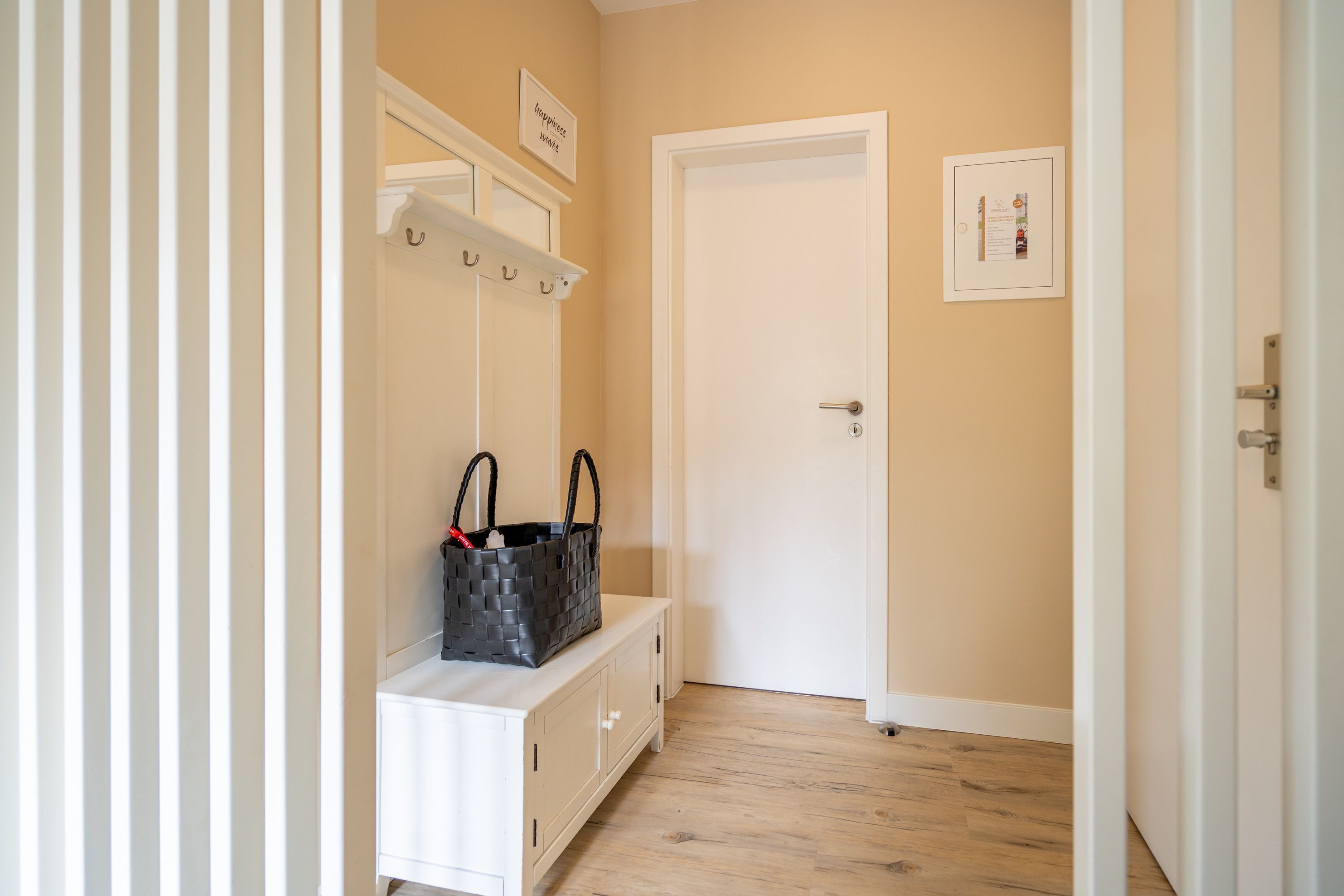 A hallway with a white bench, a coat rack, and a door.