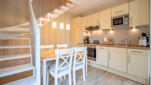 Eine moderne Küche mit einer Holztreppe, weißen Schränken und einem Essbereich mit weißen Stühlen.