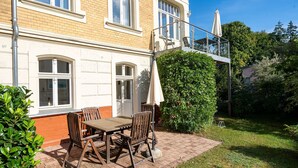 Une terrasse avec une table et des chaises, une balustrade en verre et une haie.