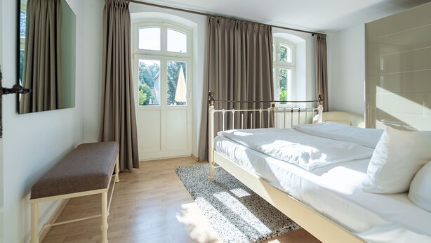 Une chambre à coucher avec un lit, un banc et de grandes fenêtres avec des rideaux.