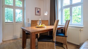 Un coin repas avec une table en bois, des chaises en osier et une vue sur la verdure grâce à de grandes fenêtres.