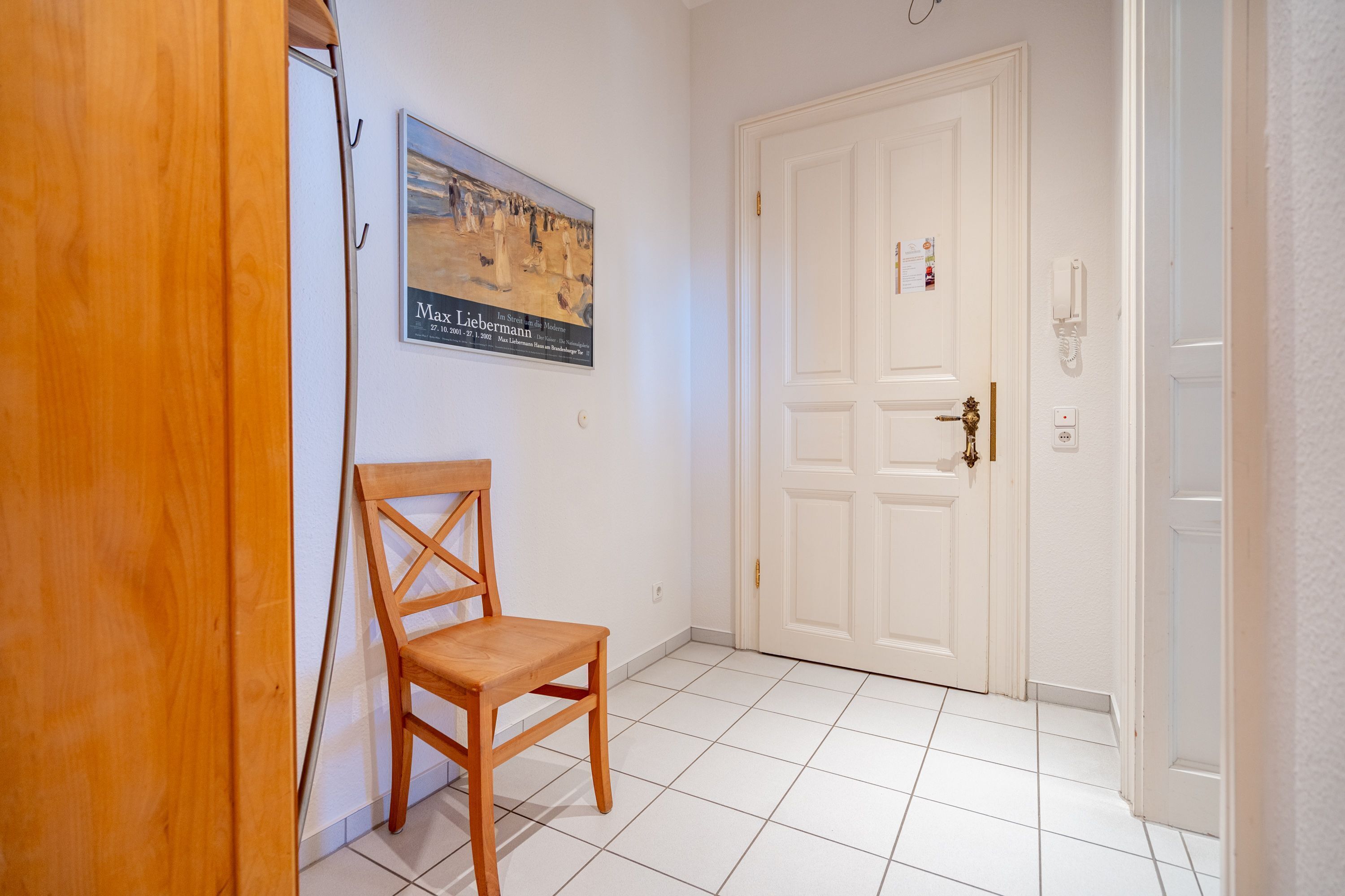 A hallway with a wooden chair, a white door, and a framed picture on the wall.