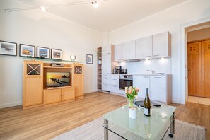 Uma cozinha moderna com armários brancos, forno embutido e área de refeições com mesa de vidro e um vaso de flores.