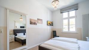 Ein Schlafzimmer mit großem Spiegel, einem Bett, einem Nachttisch, einem Sessel und einem Fenster mit Jalousien.