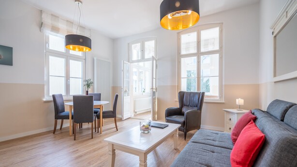 Ein modernes Wohnzimmer mit einer Couch, Sesseln, einem Esstisch und Pendelleuchten.