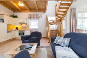 A modern kitchen with wooden cabinets, a dining area with a sofa and table, and a wooden staircase.