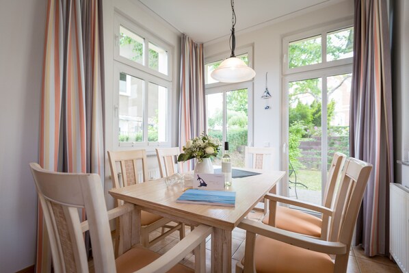 A dining area with a wooden table, chairs, a vase with flowers, and a hanging light fixture.