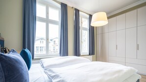 A bedroom with two beds, a large window with curtains, a wardrobe, and a hanging lamp.