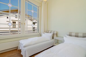 Habitación de hotel con dos camas, una mesita y una ventana que da a vista de edificios.
