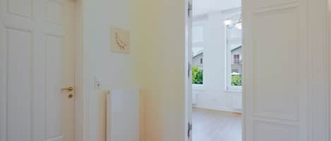 Ein Flur mit weißen Türen, einem Heizkörper und einem Fenster mit Blick auf Grünflächen.