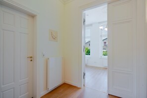 A hallway with white doors, a radiator, and a window with a view of greenery.