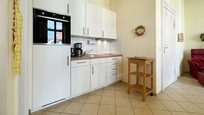 A compact kitchen with white cabinets, a built-in oven, and a small wooden table. - Villa Goodewind, App. 4 (Heringsdorf)