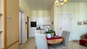 A dining area with a round table, white chairs, a vase with flowers, and a bottle of wine. - Villa Goodewind, App. 4 (Heringsdorf)