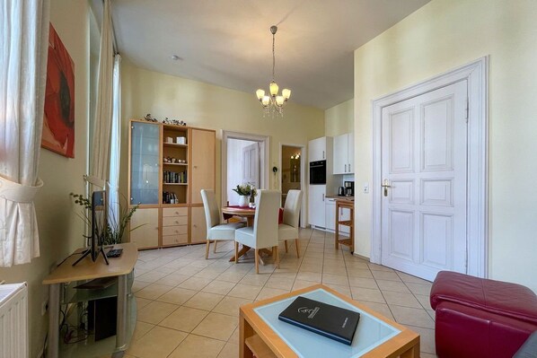 Uma sala de estar espaçosa com uma mesa de jantar, cadeiras, um sofá vermelho, uma mesa de centro de madeira e uma estante.