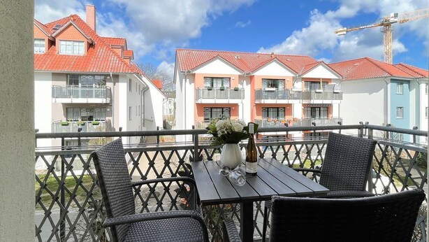 A balcony with wicker chairs and a table, overlooking a row of colorful buildings with red roofs. - Villa Goodewind, App. 4 (Heringsdorf)