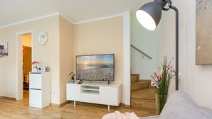 Ein Wohnzimmer mit Fernseher, einem Glastisch, einer Couch, einer Lampe und einer Treppe.