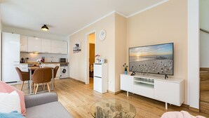 Ein modernes Wohnzimmer mit einem Glastisch, einer Couch, einem Fernseher und einer Küche im Hintergrund.