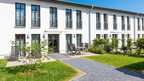 Ein modernes Gebäude mit flachem Dach, großen Fenstern und einer gepflasterten Eingangszone.