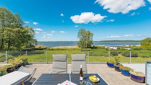 An outdoor seating area with a table, chairs, and potted plants, overlooking a lake and distant buildings. - Haus am Schmollensee, app. 7i (Heringsdorf)