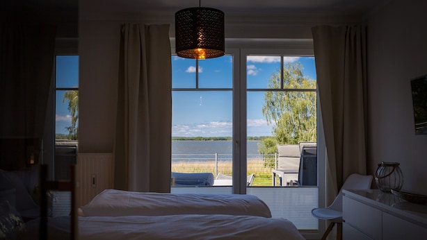 A bedroom with two beds, a view of the outdoors, and a hanging light fixture. - Haus am Schmollensee, app. 7i (Heringsdorf)
