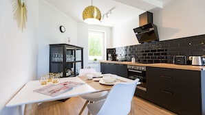 A modern kitchen with a dining area, featuring a white table, black cabinets, and a black backsplash. - Haus am Schmollensee, app. 7i (Heringsdorf)