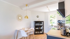 A modern kitchen with a dining area, wooden flooring, and a black bookshelf. - Haus am Schmollensee, app. 7i (Heringsdorf)