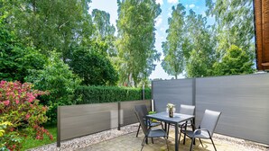 An outdoor patio with a table and chairs, surrounded by a wooden fence and lush greenery. - Maxine, Trassenheide (Baltic seaside resort), Germany (Trassenheide)